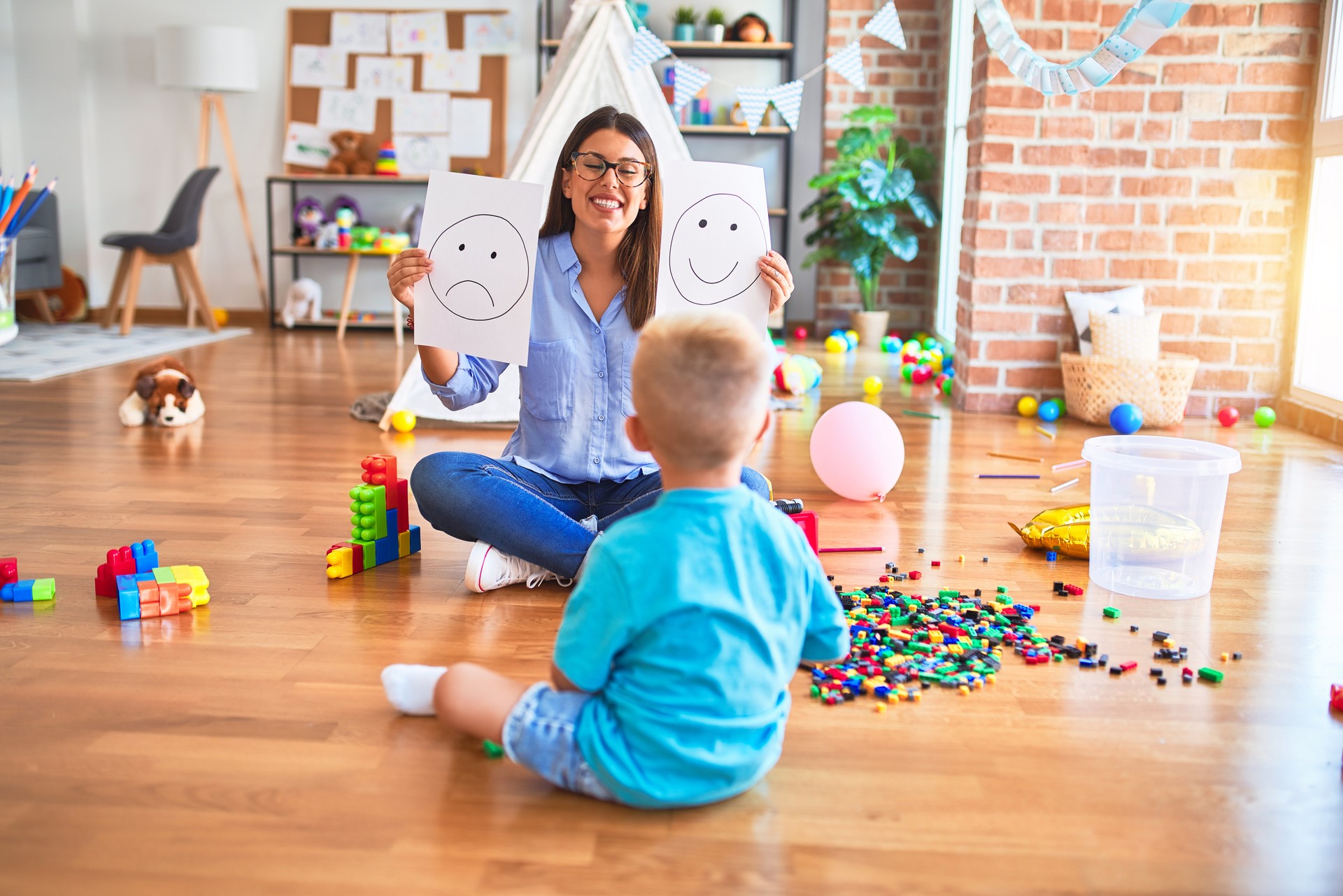 Young therapist woman speaking with child, counselor and behaviour correction at the office showing happy and sad face