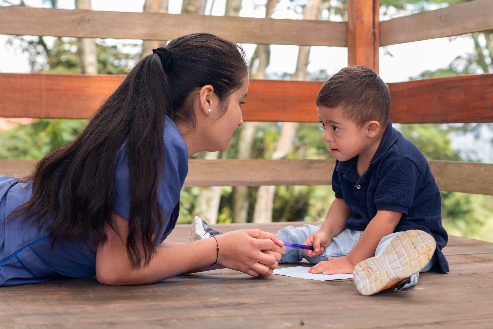 Woman in blue uniform teaching writing to a child with Down syndrome. Children's occupational therapy.